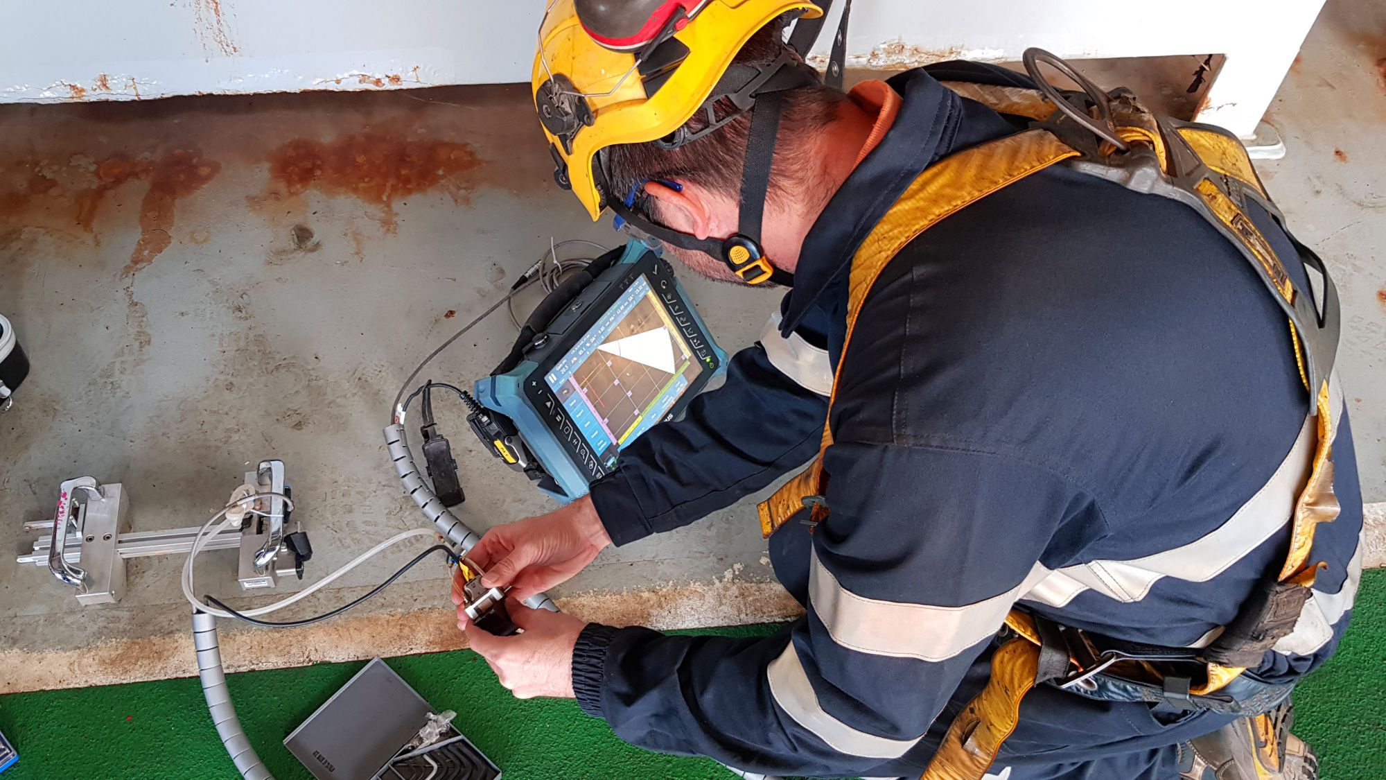 NDT technician in PPE running a phased array scan on a corroded plate